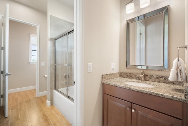 bathroom featuring baseboards, bath / shower combo with glass door, wood finished floors, and vanity