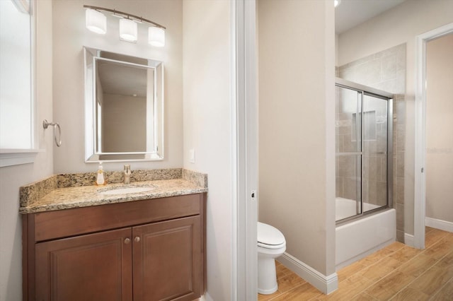 full bathroom with baseboards, bath / shower combo with glass door, toilet, wood finished floors, and vanity