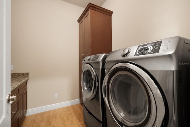 laundry room featuring light wood-style flooring, cabinet space, baseboards, and washing machine and dryer