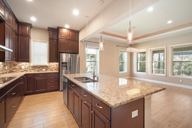 kitchen with light stone counters, light wood finished floors, a sink, appliances with stainless steel finishes, and tasteful backsplash