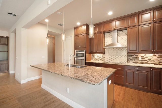 kitchen with a sink, backsplash, light wood-style floors, and wall chimney range hood