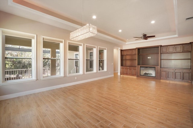 unfurnished living room featuring a ceiling fan, a tray ceiling, a glass covered fireplace, light wood-style floors, and baseboards