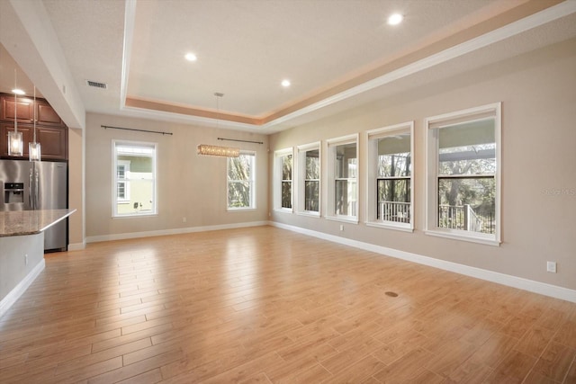 unfurnished living room featuring a raised ceiling, baseboards, visible vents, and light wood finished floors