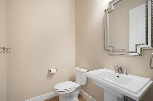 half bathroom with toilet, wood finished floors, baseboards, and a sink