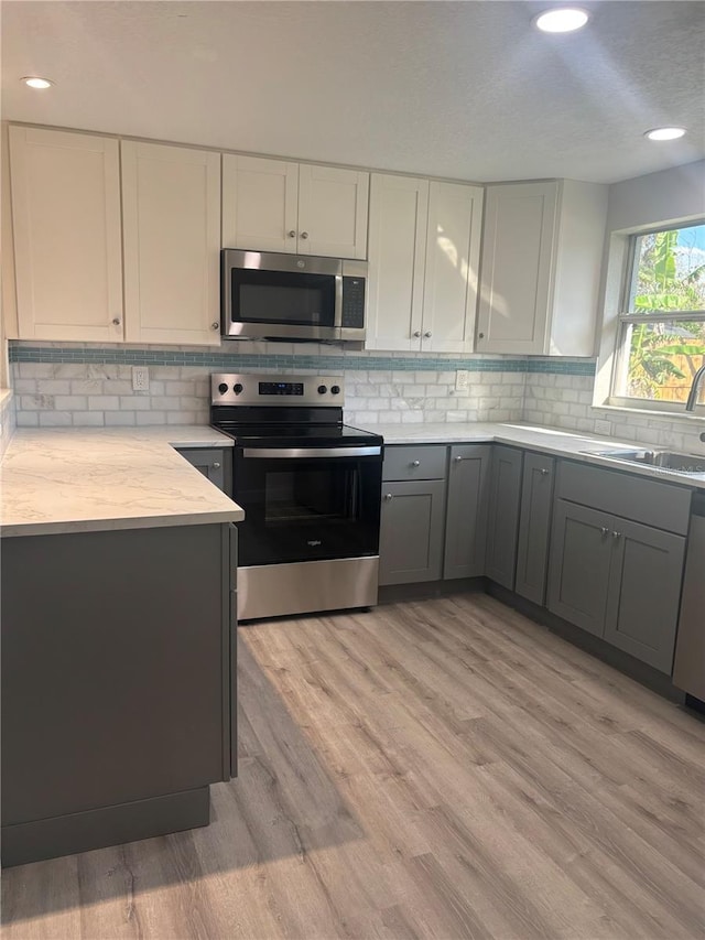 kitchen featuring light wood-style flooring, gray cabinetry, a sink, light countertops, and appliances with stainless steel finishes