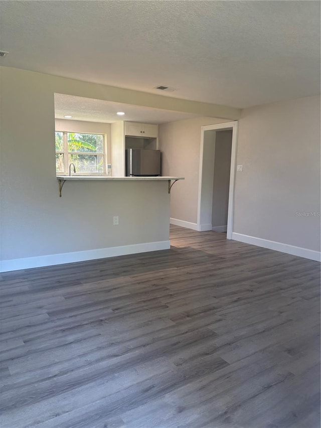 empty room featuring dark wood-style floors, visible vents, a textured ceiling, and baseboards