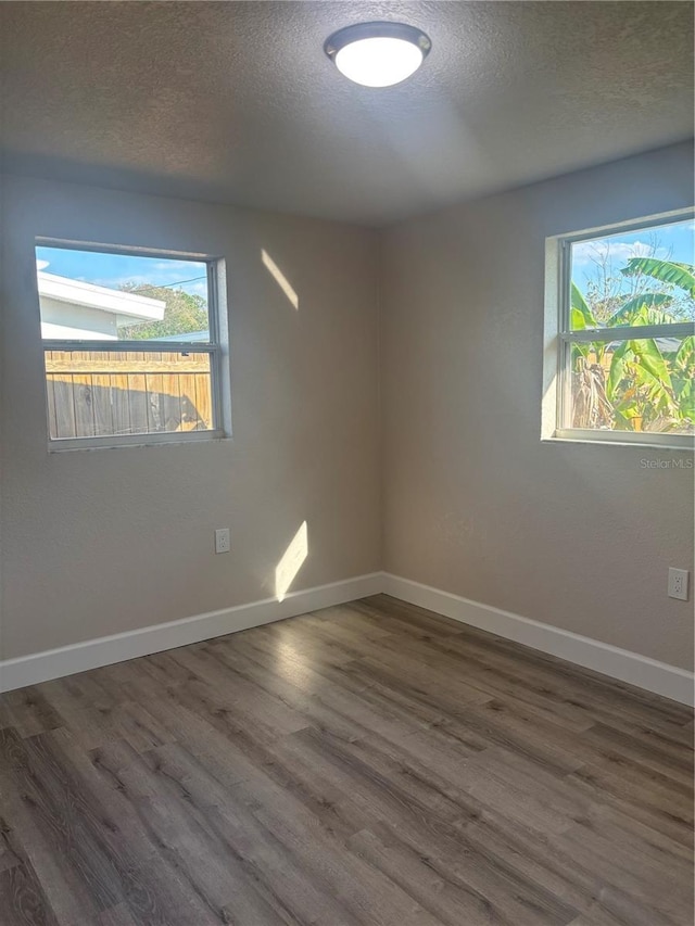 empty room featuring a textured ceiling, baseboards, and wood finished floors