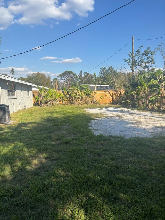 view of yard with driveway, fence, and central AC