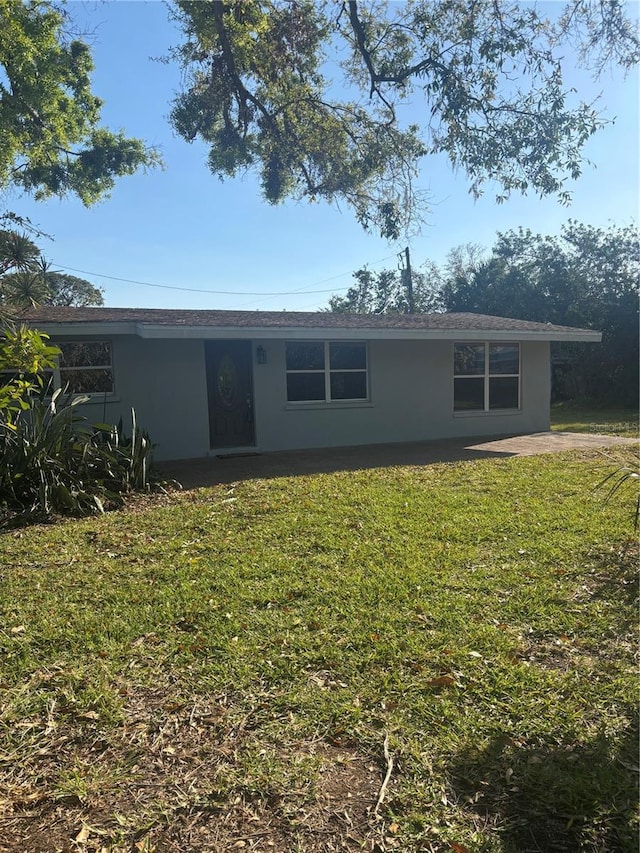 rear view of house featuring a lawn and stucco siding