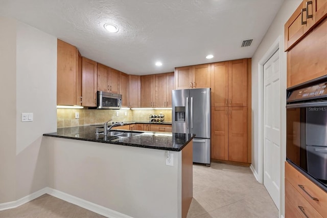 kitchen featuring stainless steel appliances, a sink, visible vents, backsplash, and dark stone countertops