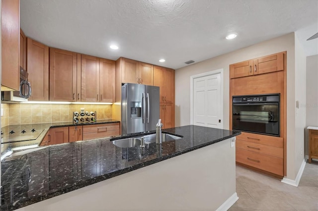 kitchen featuring visible vents, dark stone counters, backsplash, black appliances, and a sink