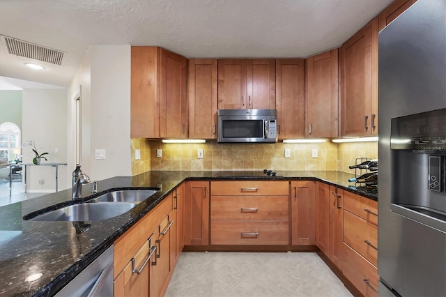 kitchen with brown cabinets, tasteful backsplash, visible vents, appliances with stainless steel finishes, and a sink