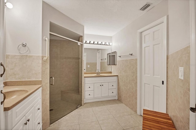 bathroom with two vanities, visible vents, a sink, tile walls, and a stall shower