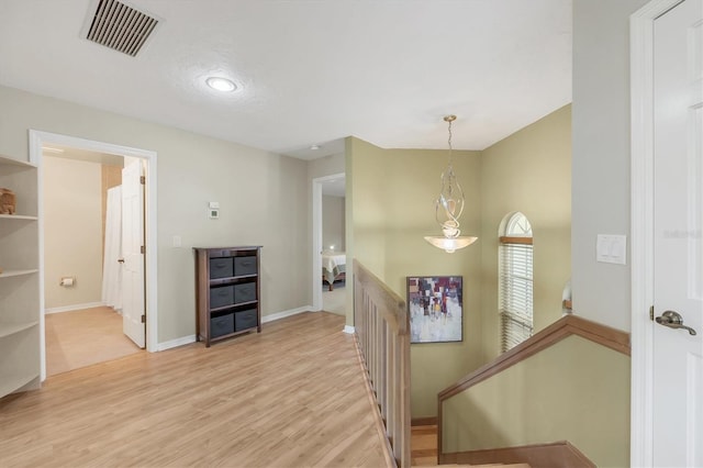 hallway featuring light wood-style floors, baseboards, visible vents, and an upstairs landing