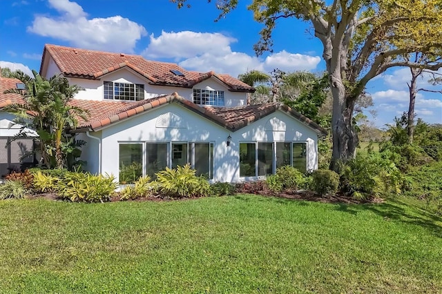 rear view of house featuring a yard, a tile roof, and stucco siding