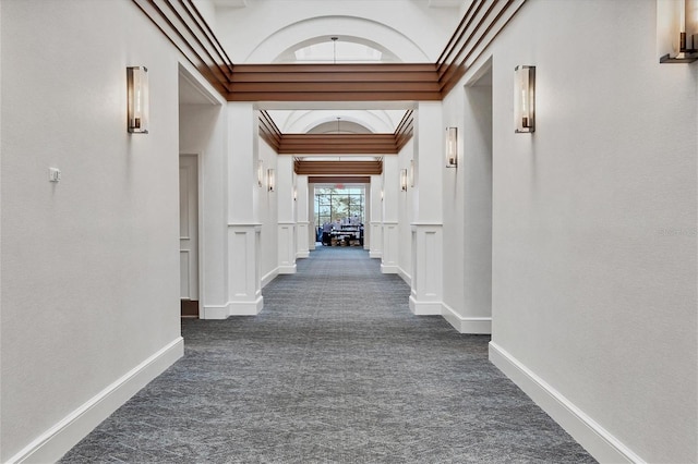 hallway with crown molding, dark colored carpet, wainscoting, and a decorative wall