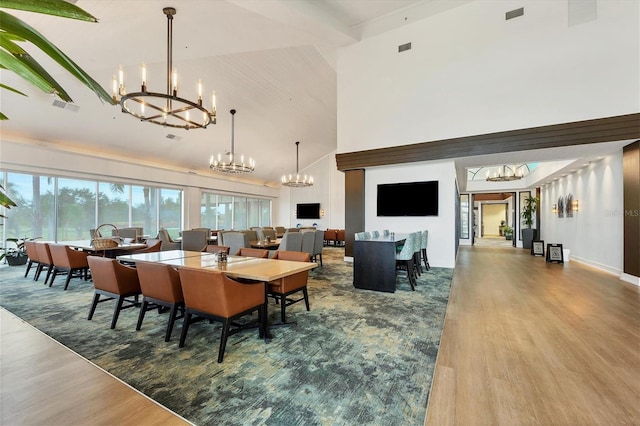 dining space with visible vents, a notable chandelier, a towering ceiling, and wood finished floors