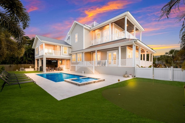 rear view of house featuring a patio, fence private yard, a balcony, a pool with connected hot tub, and a lawn