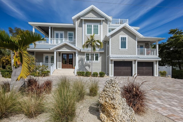 view of front of property with decorative driveway, french doors, a porch, an attached garage, and a balcony