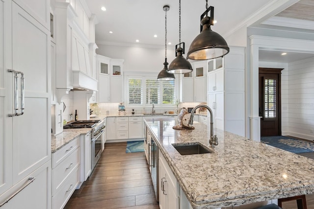 kitchen featuring a center island with sink, a sink, stainless steel stove, and white cabinetry