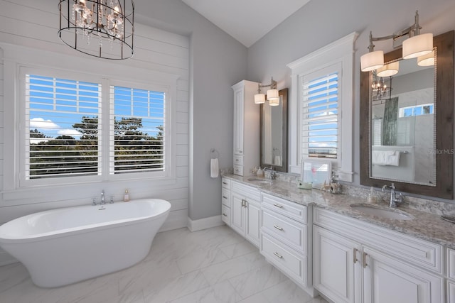 bathroom with a sink, a freestanding bath, marble finish floor, double vanity, and an inviting chandelier