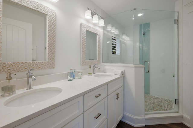 bathroom with double vanity, a shower stall, baseboards, and a sink