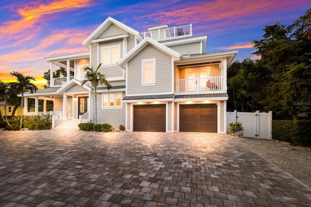 shingle-style home with a garage, a balcony, a gate, fence, and decorative driveway