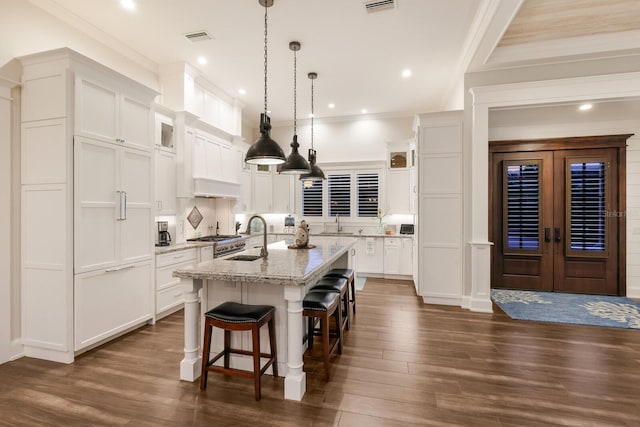 kitchen with visible vents, white cabinets, an island with sink, a kitchen bar, and a sink