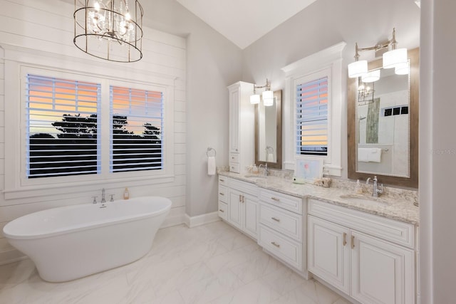 full bath with a freestanding bath, marble finish floor, double vanity, and a sink