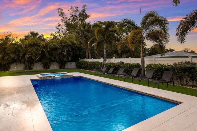 pool at dusk with a patio area, a fenced backyard, a pool with connected hot tub, and a lawn