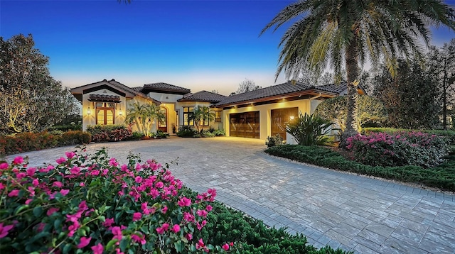 mediterranean / spanish home featuring stucco siding, a tiled roof, decorative driveway, and a garage