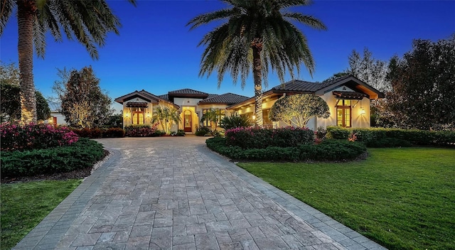 mediterranean / spanish-style home featuring stucco siding, a tiled roof, decorative driveway, and a front yard