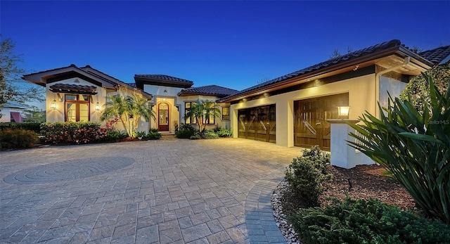 mediterranean / spanish-style house with a tile roof, decorative driveway, an attached garage, and stucco siding