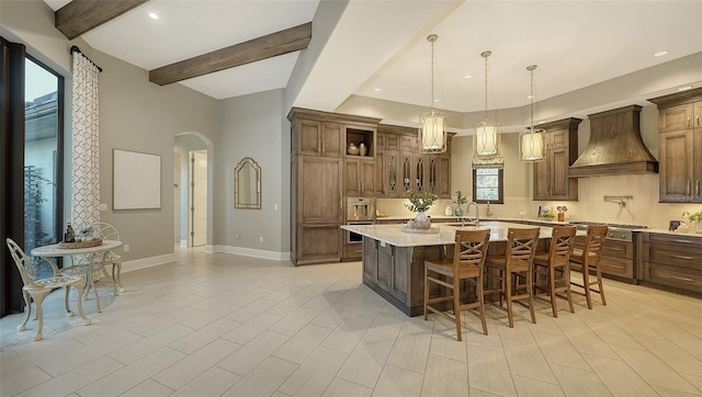 kitchen with baseboards, custom exhaust hood, beam ceiling, arched walkways, and backsplash