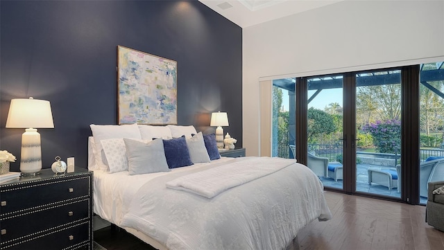 bedroom featuring access to exterior, a high ceiling, and wood finished floors