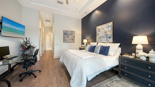 bedroom featuring wood finished floors, baseboards, visible vents, a tray ceiling, and ornamental molding