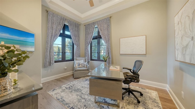 office featuring baseboards, a raised ceiling, light wood-style flooring, and a ceiling fan