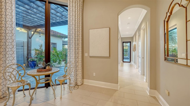 corridor with light tile patterned floors, baseboards, arched walkways, and ornamental molding