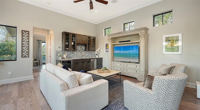 living room with beverage cooler, wood finished floors, crown molding, baseboards, and a towering ceiling