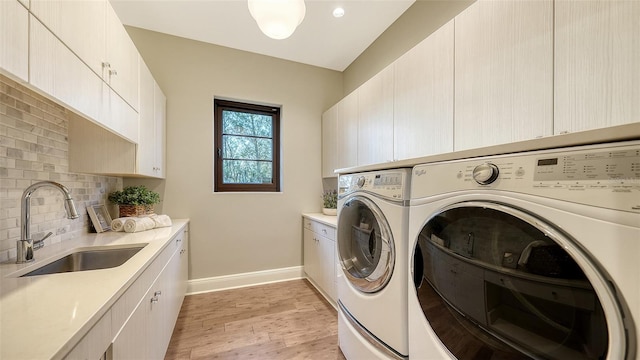 laundry room with light wood finished floors, baseboards, separate washer and dryer, cabinet space, and a sink