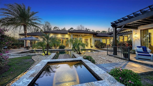 back of house at dusk featuring a tiled roof, a patio area, an outdoor pool, and stucco siding