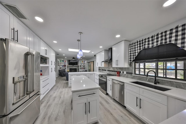 kitchen featuring a fireplace, stainless steel appliances, visible vents, a sink, and wall chimney range hood