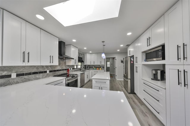 kitchen featuring wall chimney range hood, white cabinetry, appliances with stainless steel finishes, and a sink