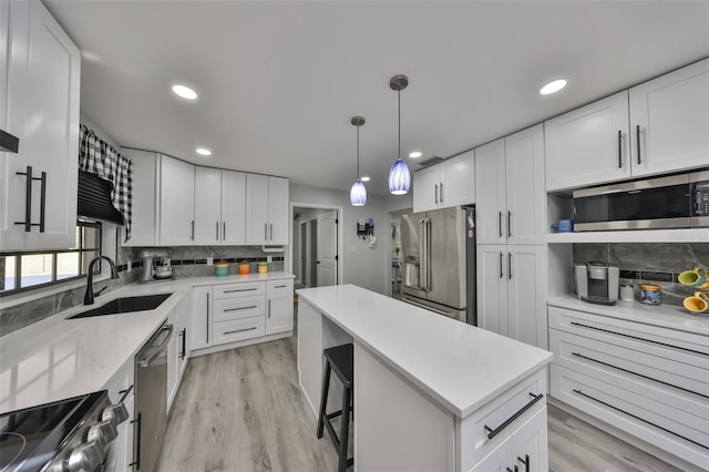 kitchen with stainless steel appliances, a sink, white cabinetry, decorative backsplash, and a center island