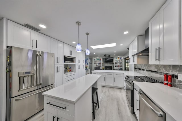 kitchen featuring a skylight, visible vents, wall chimney exhaust hood, appliances with stainless steel finishes, and white cabinetry