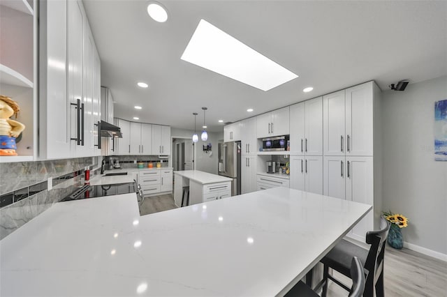 kitchen with under cabinet range hood, stainless steel appliances, a peninsula, a skylight, and tasteful backsplash