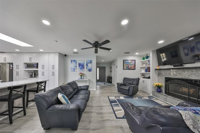 living area featuring recessed lighting, a fireplace, a skylight, baseboards, and light wood-type flooring