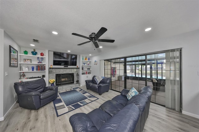 living area featuring a textured ceiling, a stone fireplace, wood finished floors, and visible vents