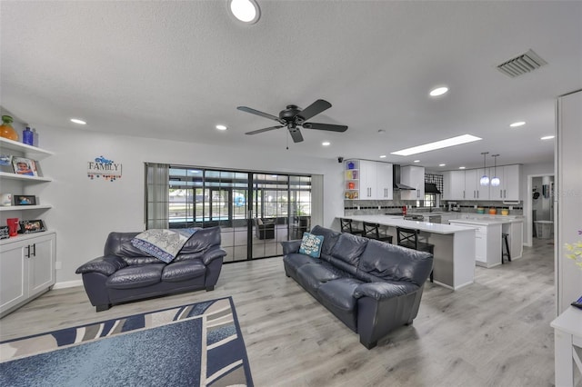 living room featuring light wood finished floors, a skylight, visible vents, and recessed lighting