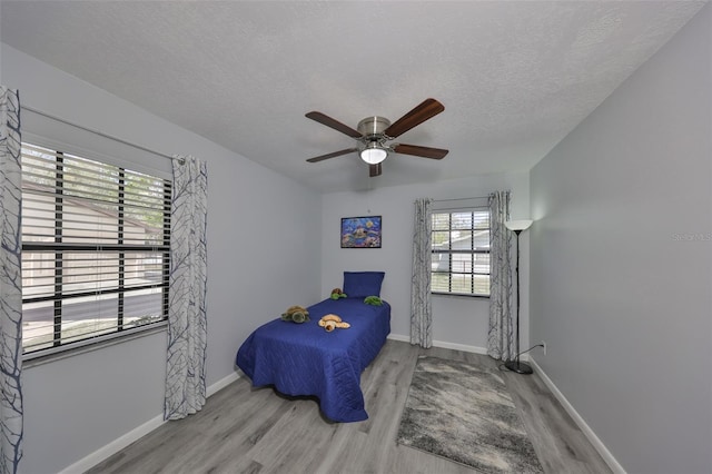 bedroom featuring ceiling fan, a textured ceiling, baseboards, and wood finished floors